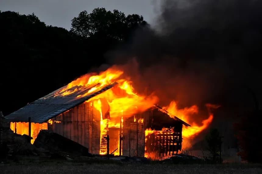 Wood-frame structure engulfed in flames at dusk, fire damage claim